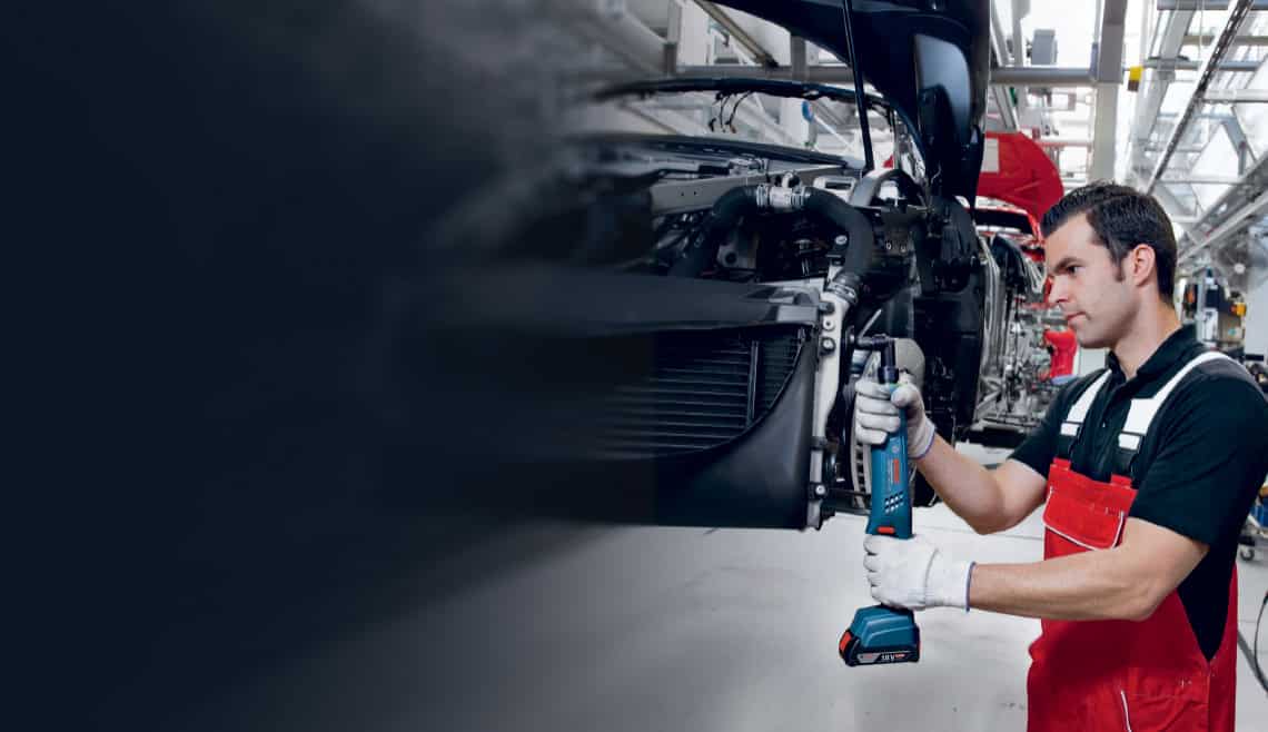 Operator using Bosch Rexroth Exact cordless screwdriver for precise tightening in automotive production line with real-time data monitoring.