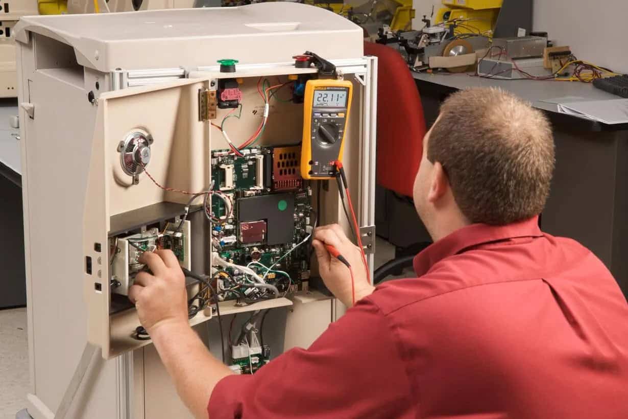 Maintenance engineer using Fluke 179 Digital Multimeter for industrial control panel troubleshooting.