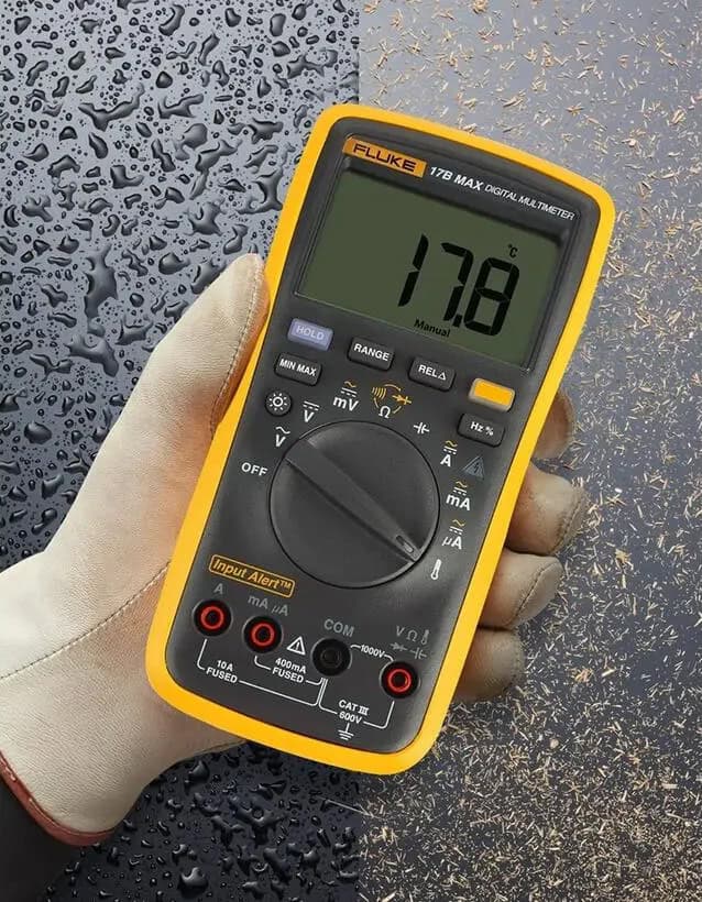 Close-up การทดสอบความทนทานของมัลติมิเตอร์ Fluke 17B MAX แสดงหยดน้ำและฝุ่นไม้บนตัวเครื่องเพื่อยืนยันมาตรฐานงานหนัก