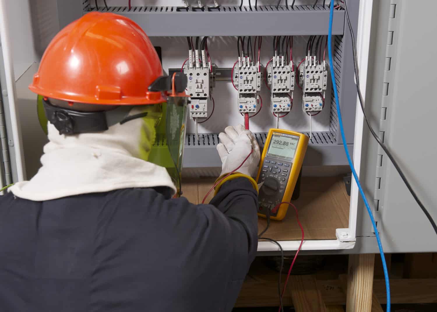 A professional electrician in full safety gear performing a final system check with a Fluke multimeter, summarizing the importance of precision and safety in industrial electrical work.