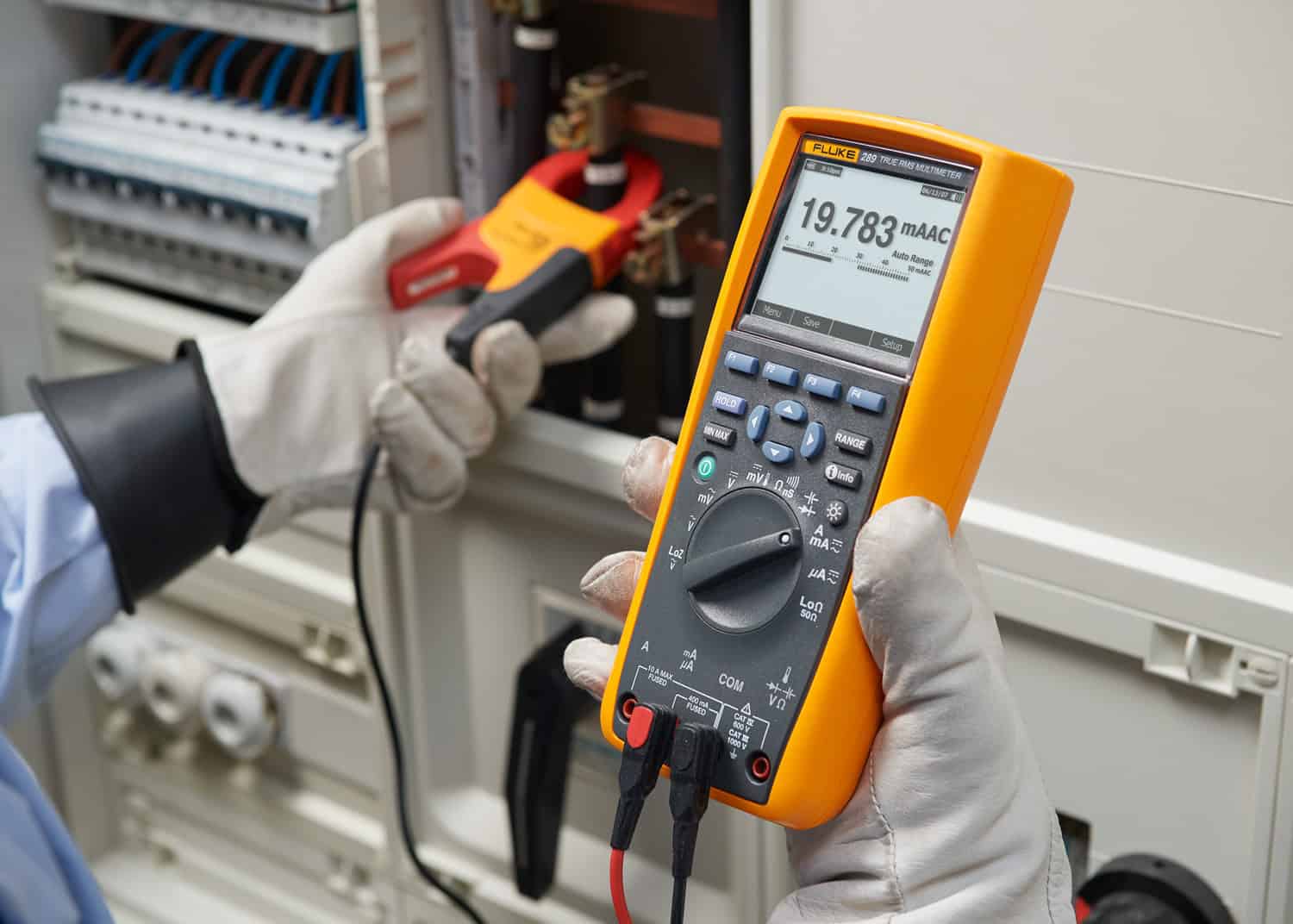 A professional electrician using Fluke 289 True-RMS Industrial Multimeter and a clamp probe to troubleshoot a complex electrical control panel, demonstrating heavy-duty field maintenance.