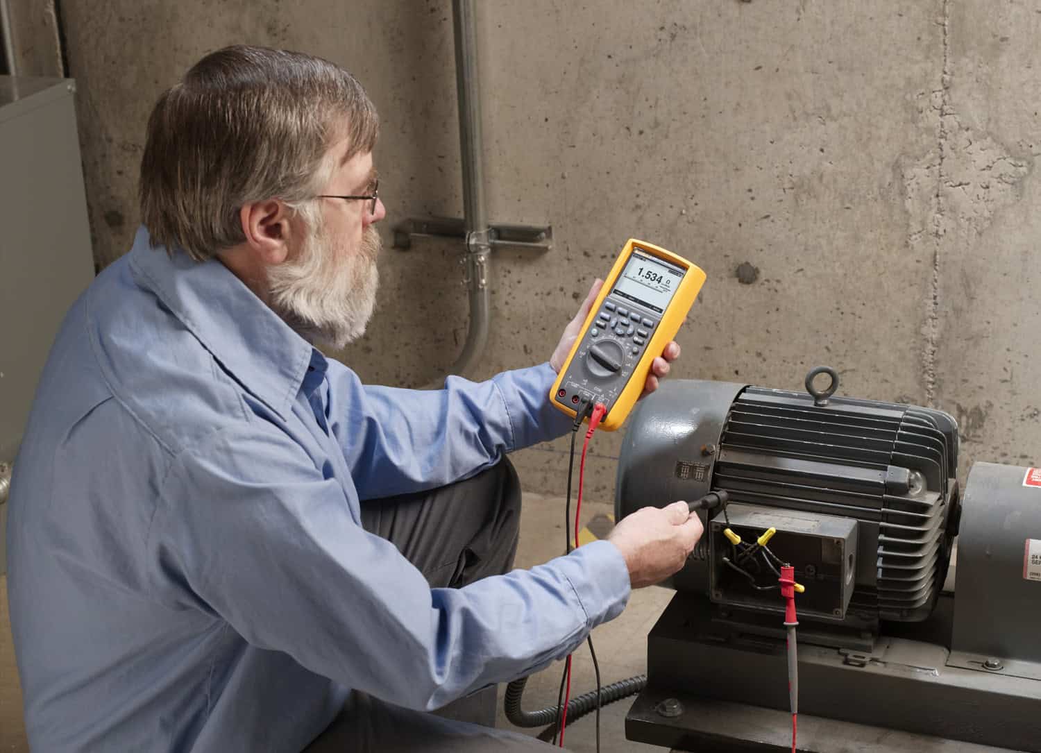 A technician using the Fluke 289 True-RMS Industrial Logging Multimeter to measure and diagnose an electric motor in a plant environment, showing real-world industrial maintenance application.