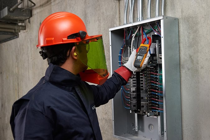 Electrician wearing safety PPE while using Fluke 376 FC clamp meter on an industrial electrical panel